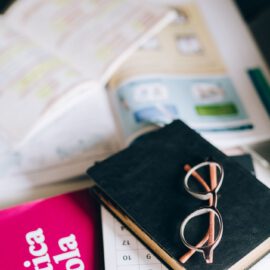 A study setup with a Spanish grammar book, calendar, and eyeglasses on a desk, suggesting focused learning.